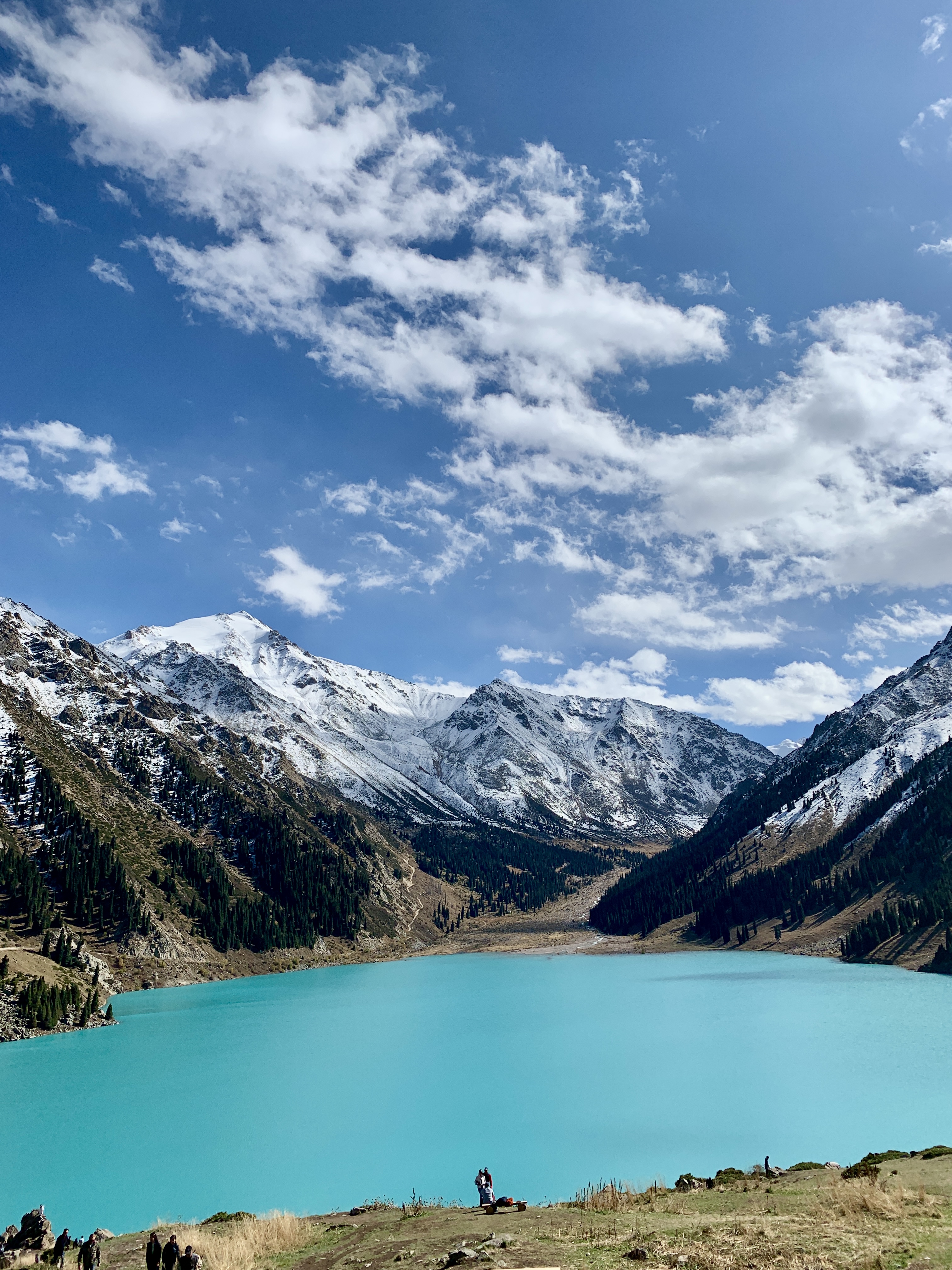 Turquoise Big Almaty Lake beneath dramatic clouds and mountain peaks