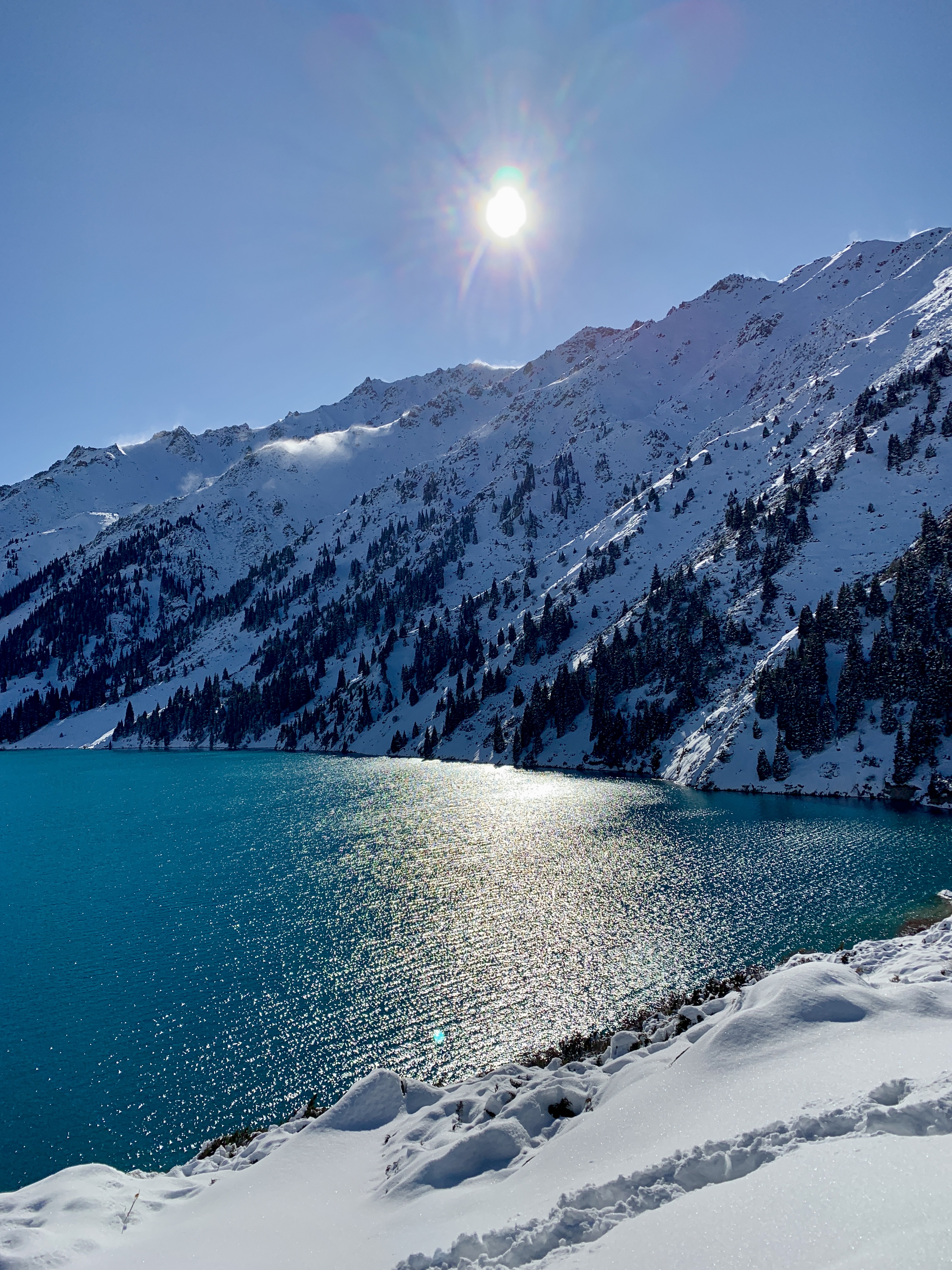 Winter sun reflected on Big Almaty Lake beside snowy slopes