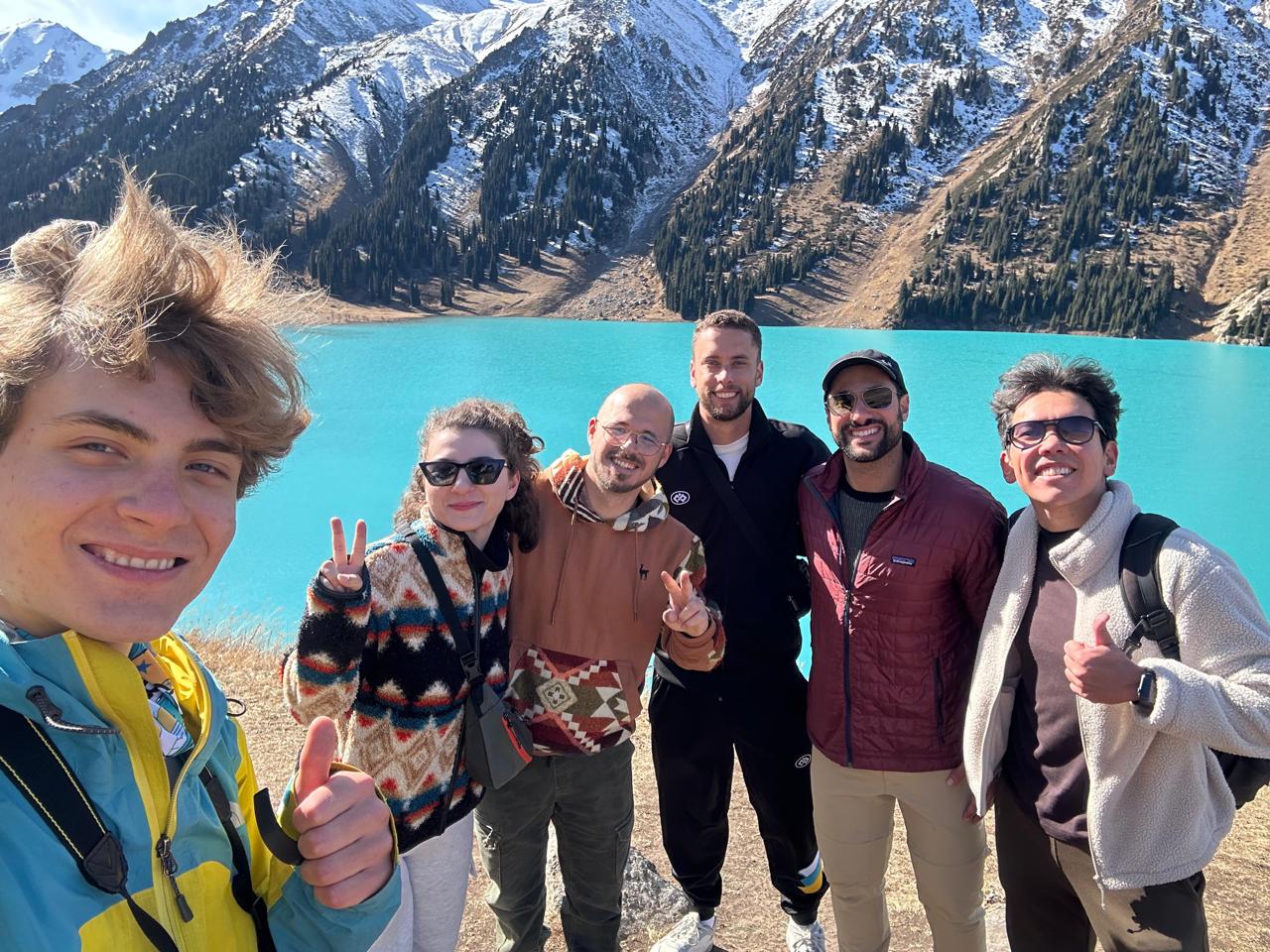 A joyful group with their guide beside turquoise Big Almaty Lake